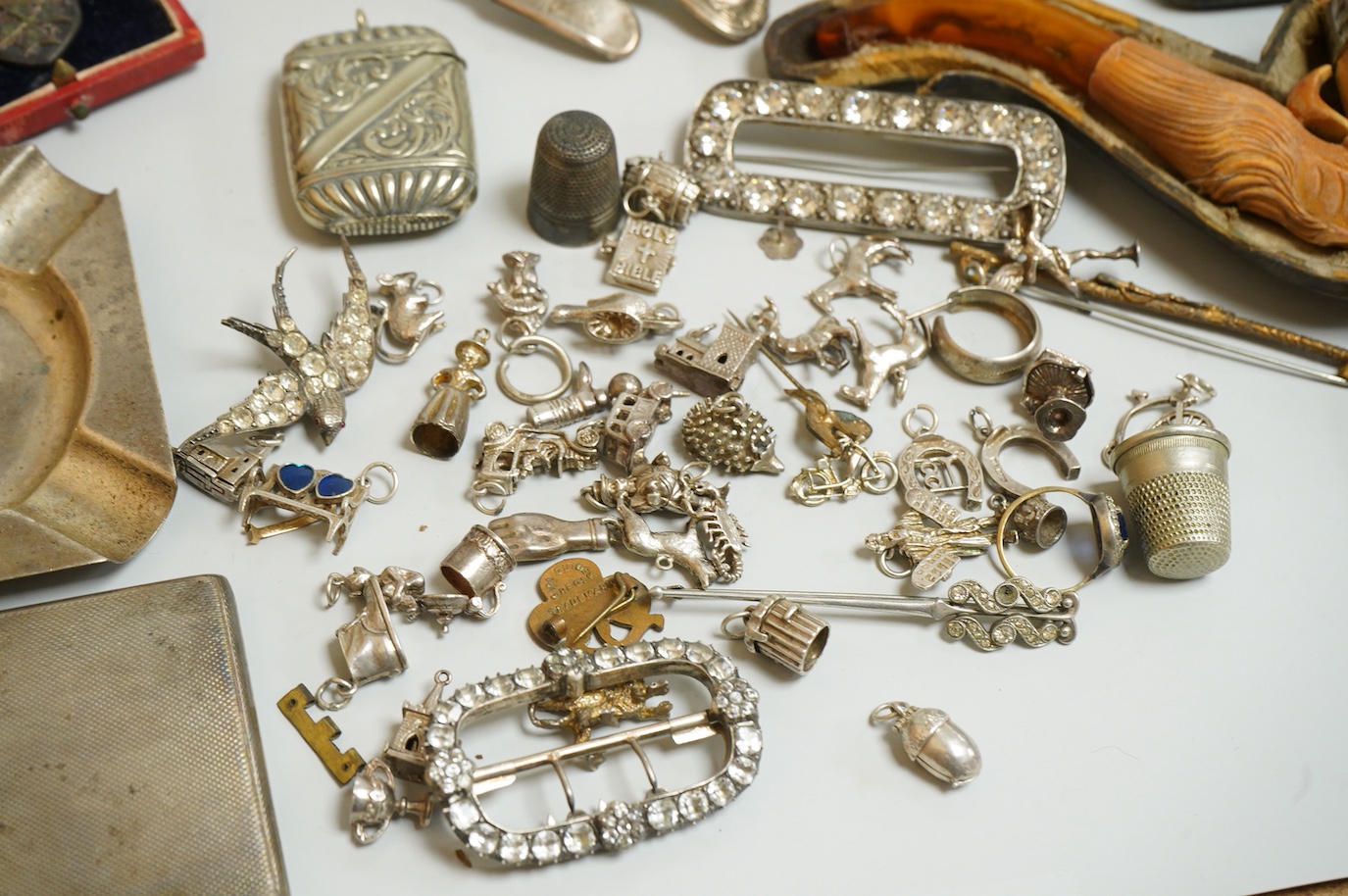A small collection of silver and white metal charms, including Holy Bible, Penny Farthing, hedgehog and squirrel, together with a silver compact and ashtray, a silver and paste brooch, nut vesta, pipe, etc.